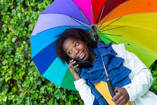 utilizzo di cellulari sotto la pioggia - candid women african descent umbrella foto e immagini stock