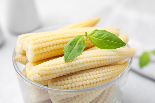 Canned baby corns with basil on white table, closeup
