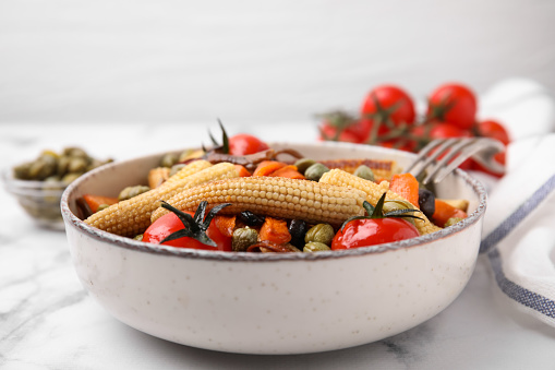 Tasty roasted baby corn with tomatoes and capers on white marble table, closeup