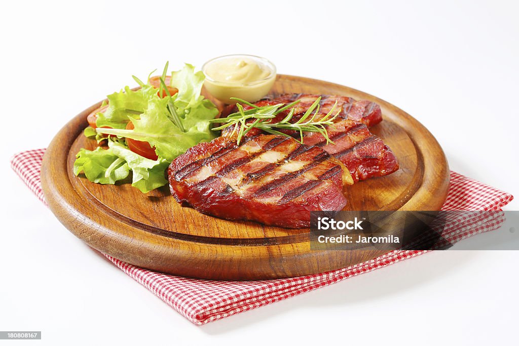 Grilled pork neck on a round cutting board Slices of grilled pork neck with mustard and salad on a round cutting board Appetizer Stock Photo