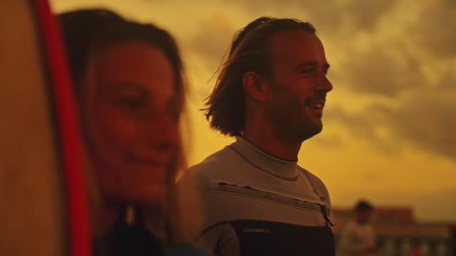 Happy surfer couple talking and laughing on sunset beach