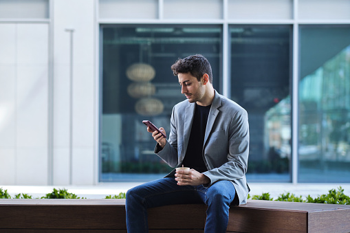 side view portrait of a white generation z man doing a break from work and talking by the phone and drinking coffee outdoors