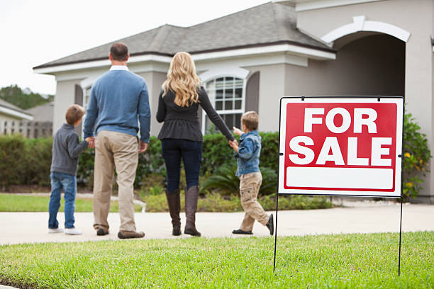 Family looking at house for sale Family with two boys (4 and 6 years) standing in front of house with FOR SALE sign in front yard.  Focus on sign. for sale sign photos stock pictures, royalty-free photos & images