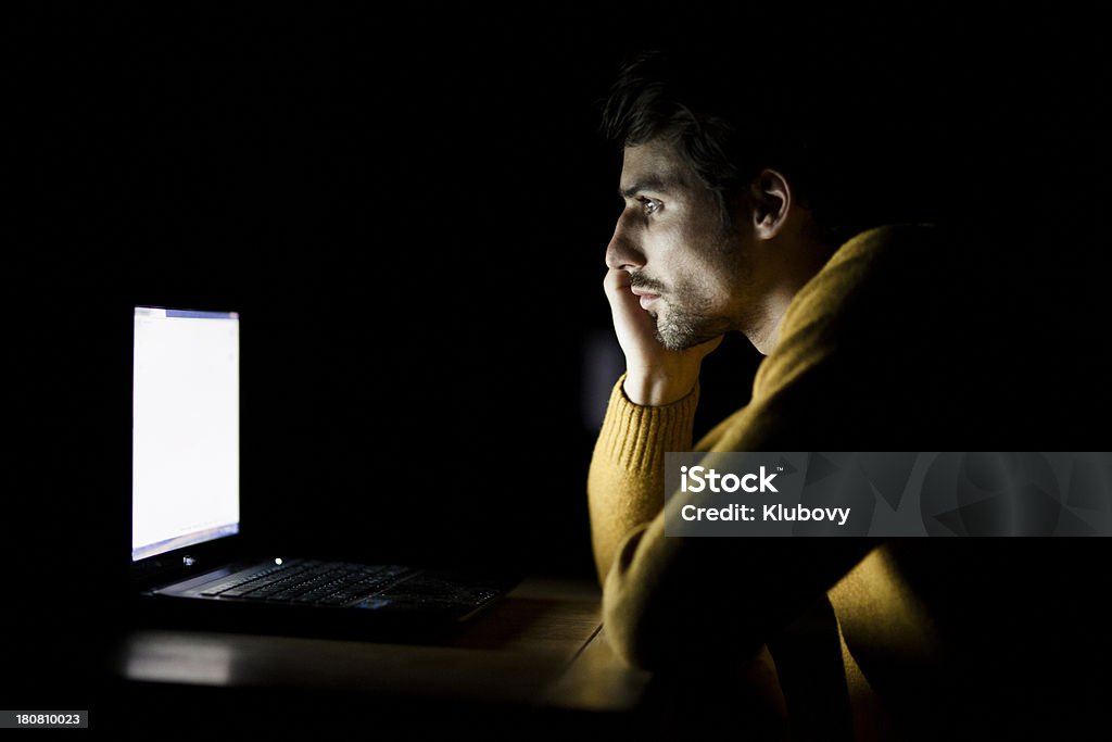 Late night working on laptop Low key portrait of a young handsome man working on laptop late into the night. Staring Stock Photo
