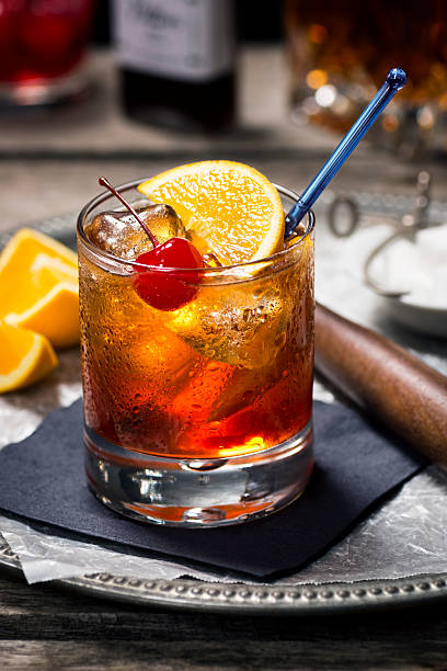 Image of old fashioned cocktail with fruits on black napkin The Old Fashioned is most commonly made by muddling sugar cubes with bitters, a cherry and an orange wedge or peel. Usually a splash of water or soda water is added along with ice, bourbon (or rye) and a garnish.  maraschino cherry stock pictures, royalty-free photos & images