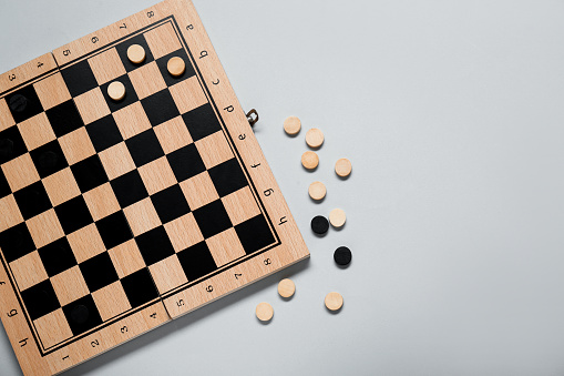 Wooden checkerboard and game pieces on light grey background, flat lay. Space for text