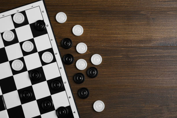 istock Checkerboard and game pieces on wooden table, flat lay. Space for text 1808121509