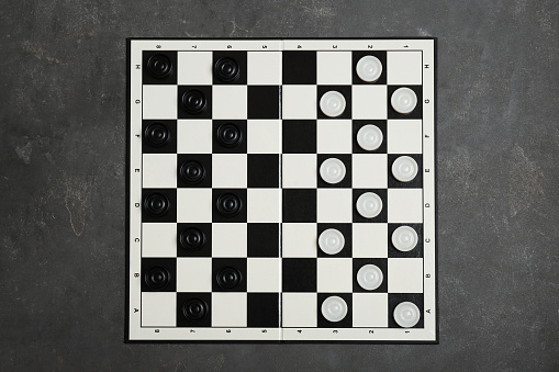 Checkerboard with game pieces on grey table, top view