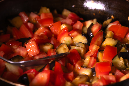 Close-up of tomatoes and eggplants fried in a frying pan. Mixing ingredients with a spoon in a frying pan. Cooking process