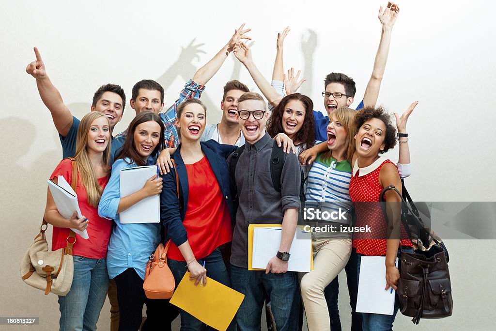Large group of happy students Large group of diverse high school students standing against white wall, embracing, raising hands and laughing at camera.  Book Stock Photo