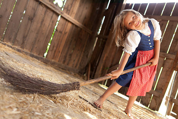 happy young girl dressed in dirndl brooming in wooden barn