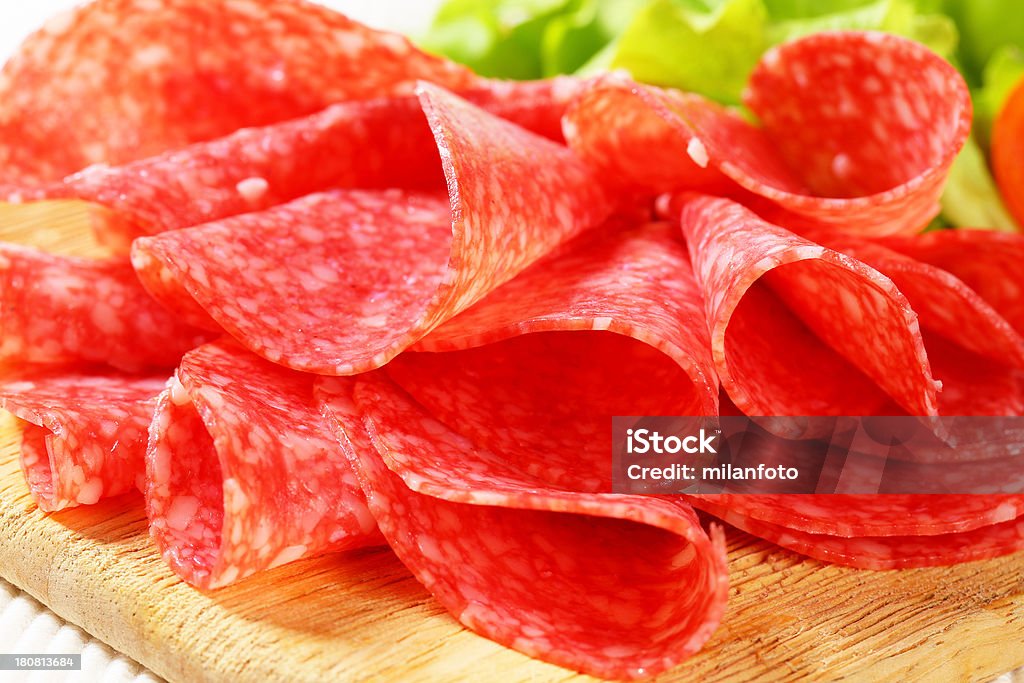 sliced salami heap of folded salami slices on a wooden cutting board Chopped Food Stock Photo