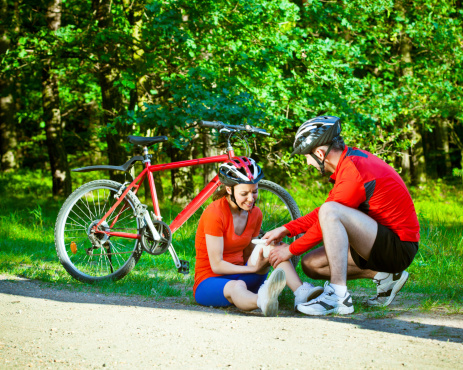Woman fell the bike, man bandaging her knee.