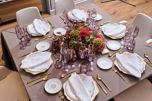 High angle of various dishware and cutlery served with glassware and placed on banquet table decorated with blooming flowers