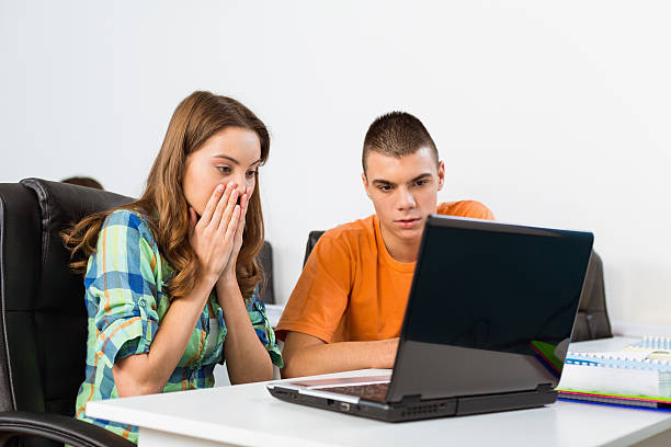 Two teenagers looking at a laptop with surprise