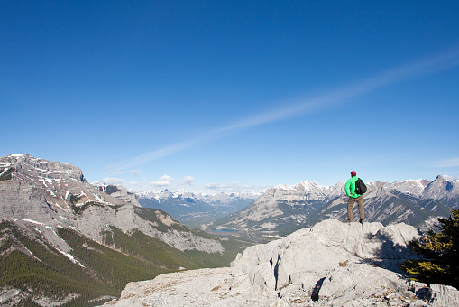 A hiker standing on the summit of a mountain. Horizontal colour image. An unrecognizable male in his 30s standing on a summit in the Canadian Rockies. This is the summit of Heart Mountain, which is one of the first peaks you get to west of Calgary. Themes include hiking, trekking, climbing, alpine, scrambling, adventure, adventurer, mountaineering, and recreation. Self portrait shot with tripod and self timer. 