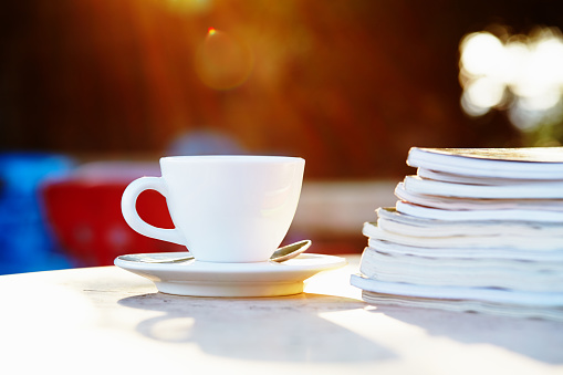 Cup of coffee and magazines on the table at the outdoor cafe with creamy bokeh at the background