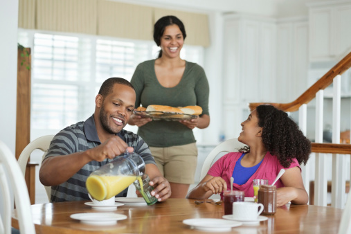 Happy mother bringing breakfast for family sitting at table in domestic room