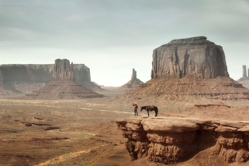 Subject: A native American Indian cowboy with his horse over a cliff looking into the distance.