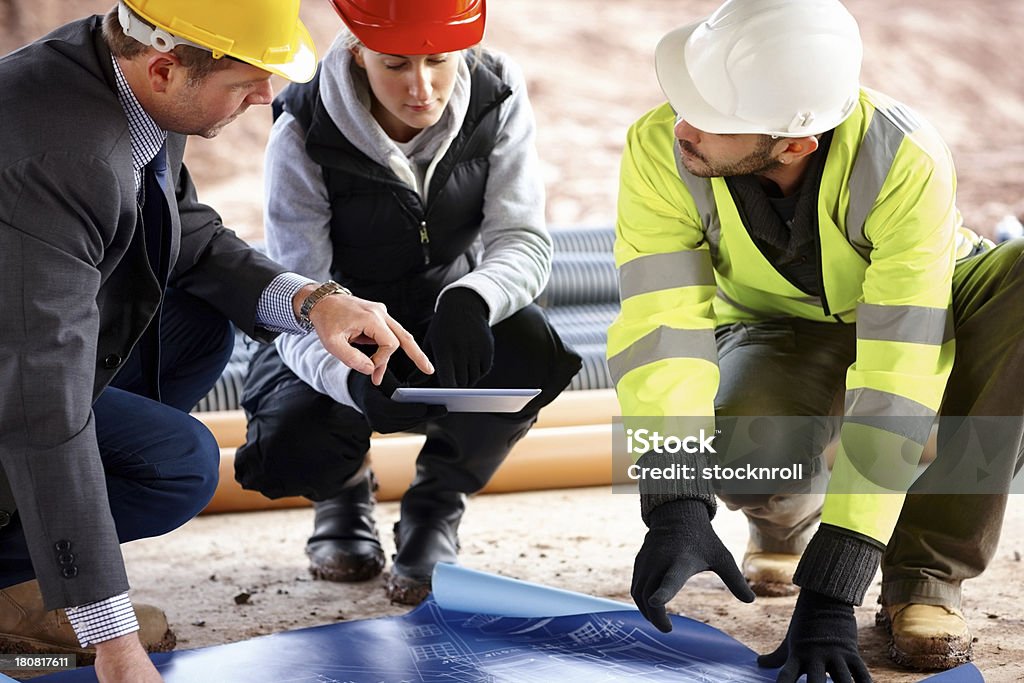 Trabajador de la construcción mirando blueprints - Foto de stock de Accesorio de cabeza libre de derechos