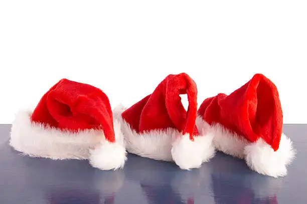 Three Santa Claus Christmas hats on table.