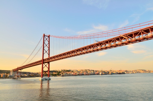The 25 de Abril Bridge across the Tagus riger in Lisbon is modeled after the Golden Gate Bridge and could pass for its twin. Here it is reaching across the Tagus river as the sun fades and lends a golden aura to the city