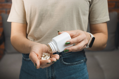 Young woman holds white medical capsules and pills in a hand, take medicine from a bottle, close-up view.