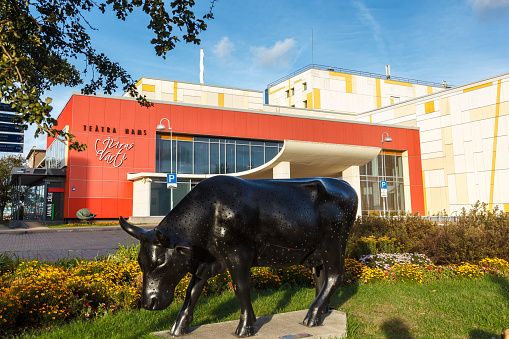 VENTSPILS, LATVIA - SEPTEMBER 21, 2019: Theatre House Juras varti with black cow in front. The cow was created by the artist Mārīte Guščika from Riga, Latvia. The name of the work is Piena Ceļš (Milky way) and it was created as part of the Cow Parade 2012, which took place in Ventspils in 2012.