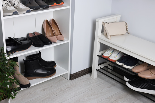 Shelving unit and shoe storage bench near white wall in hallway. Interior design