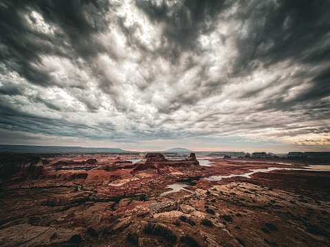 A scenic view of a large rocky mountain landscape with the Lake Powell and clouds in the sky on an overcast day