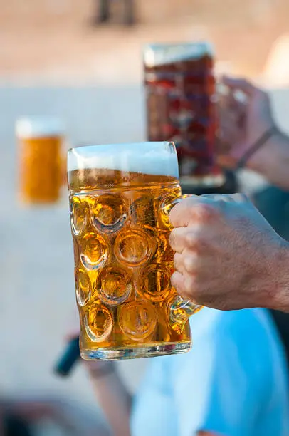 Three men with arms outstretched and holding draft beer in Taybeh, Palestine. They are engaged in a contest to see who can hold their arm out the longest.