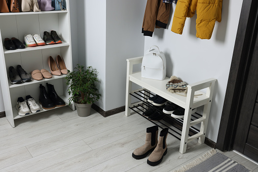 Shelving unit and shoe storage bench near white wall in hallway. Interior design