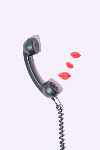 Sending kisses through a vintage handset on a pink background. Long-distance love, Valentine's concept.