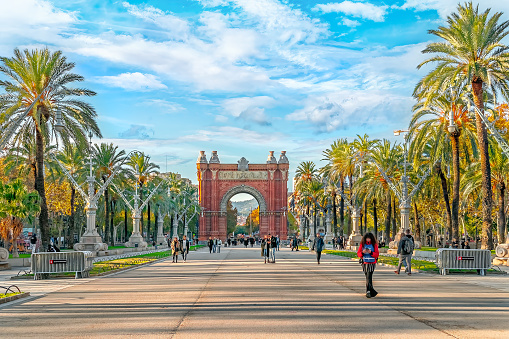 Barcelona, Spain - November 26, 2021: Passeig de Lluis Companys street and Arc de Triomphe in Barcelona on a sunny autumn day. People walk along a pedestrian tourist street in the capital of Catalonia