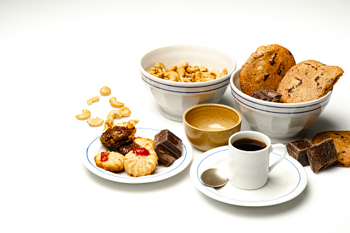 Time for a black coffee at home in the kitchen table with delicious cookies , cashews and dark chocolate .