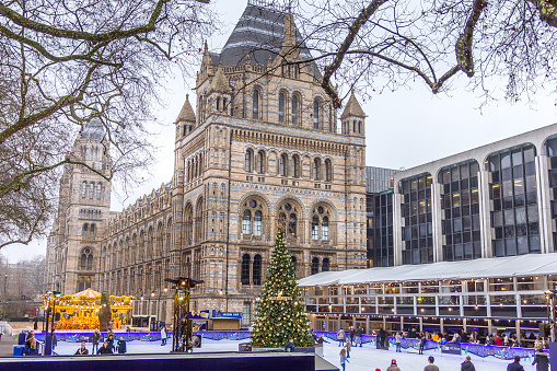 London, England - 17 December, 2016: People in the Christmas skating rink by the Natural History Museum. The famous museum is one of the various city places with holiday decoration and attractions.