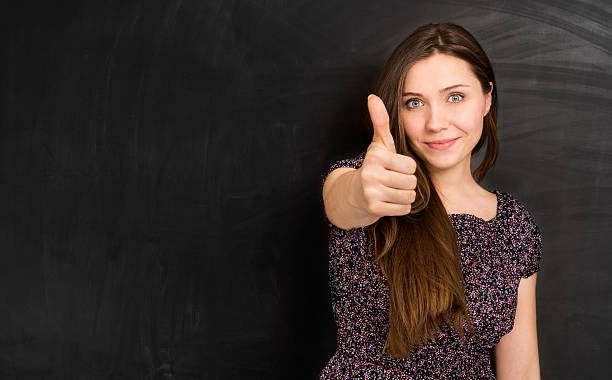 Young beautiful woman making Thumb up in front of a blackboard.
