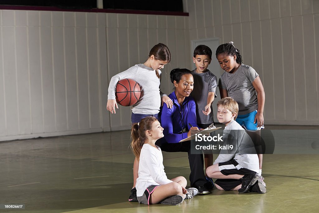 Children with basketball coach Children (7-9 years) with basketball coach (30s) in gym. African Ethnicity Stock Photo