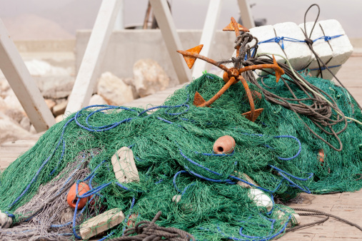 Fishing net with floats and rusty anchor on the dock
