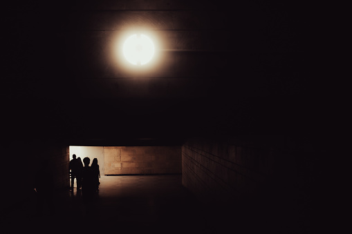 Silhouette of a group of people walking through the underground passage and a daylight coming through an entrance