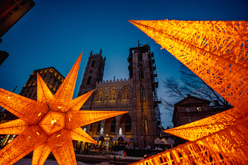 Montreal, Quebec, Canada - February 26, 2023: Notre-Dame basilica taken on a gloomy winter evening with decorative orange lightings and some unrecognizable people in the foreground