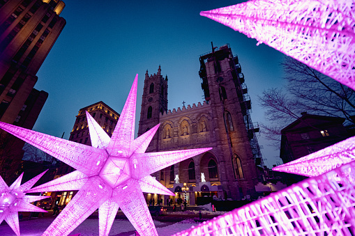 Montreal, Quebec, Canada - February 26, 2023: Notre-Dame basilica taken on a gloomy winter evening with decorative dark pink lightings and some unrecognizable people in the foreground