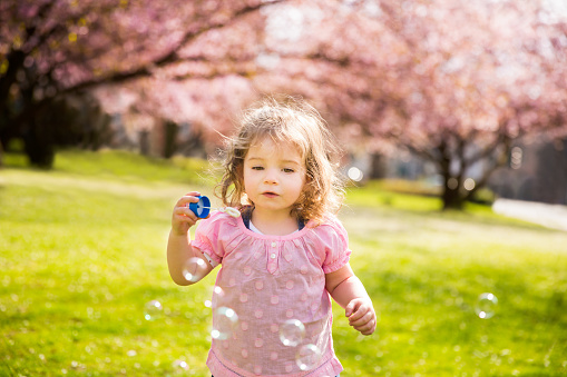 Cute girl amazed by soap bubbles in the park