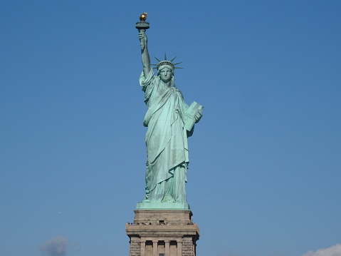 The Statue of Liberty in New York rises majestically over the glittering skyline as bright blue skies transform her into a living symbol of freedom and hope. The imposing monument sits atop Liberty Island and welcomes visitors with sublime splendor.