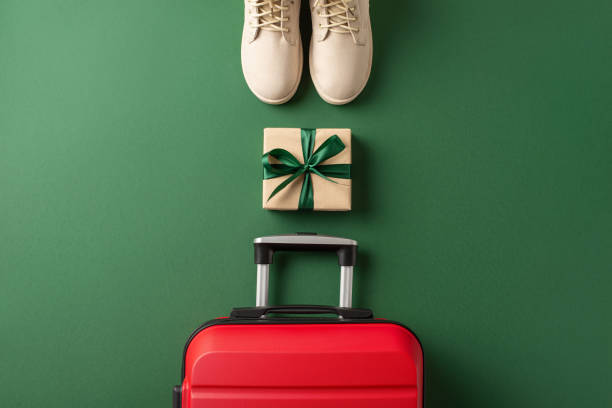 istock A journey to your dream winter vacation is symbolized by top view white boots, a suitcase, and kraft paper gift box with ribbon bow against green background. Create your winter memories here 1808334367