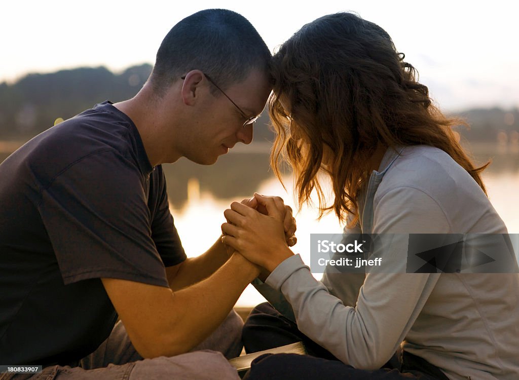 Couple Praying Together Couple praying together at sunrise by lake Praying Stock Photo