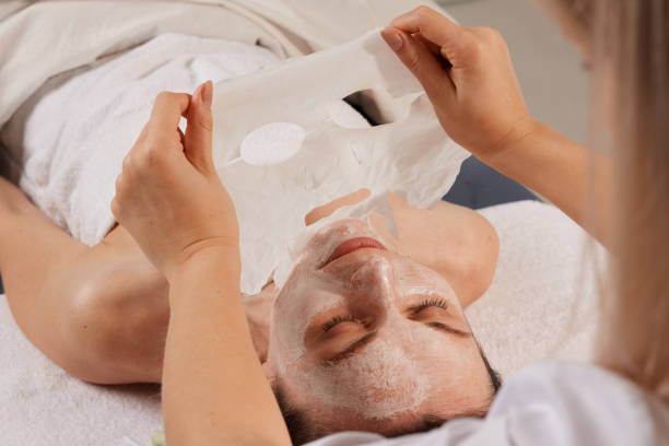 la esteticista suaviza la mascarilla en la cara de la mujer para rehidratar la piel de la cara, procedimiento cosmético antiarrugas en el salón de spa de belleza. cosmetóloga aplicando mascarilla hidratante en el rostro femenino - rehydrate fotografías e imágenes de stock