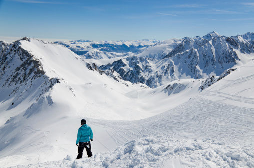There are snow slopes of mountains from the pass of Tourmalet in the winter Pyrenees. A skier is standing above the downhill.