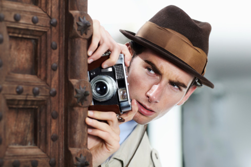 Private detective capturing a photo suspiciously from around a corner while using a retro camera