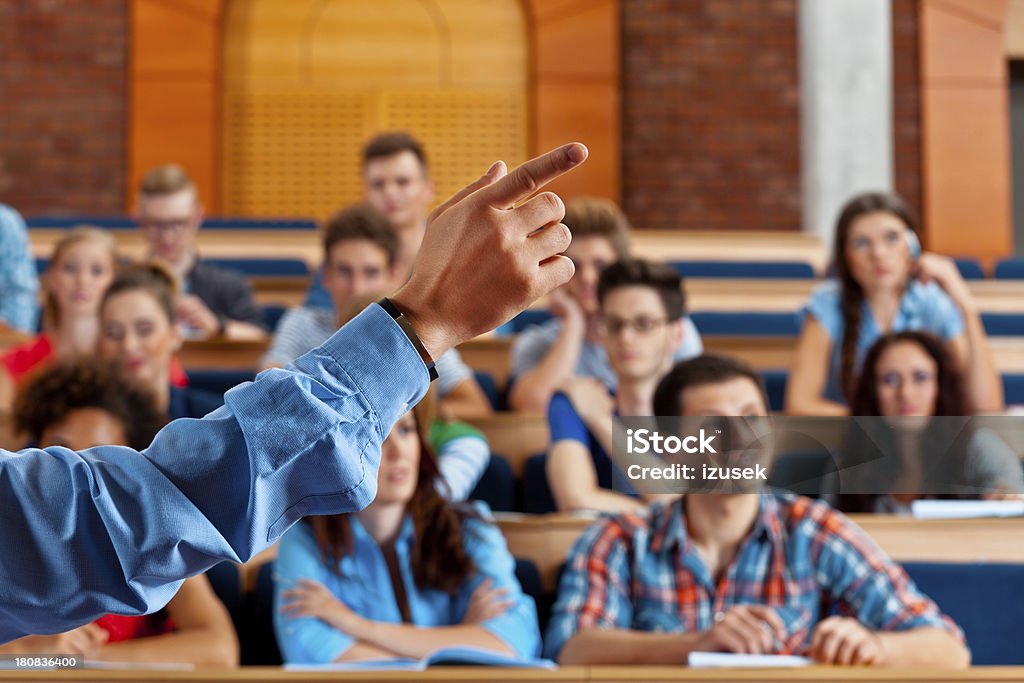 Seminar in lecure hall Large group of students sitting in the lecture hall at university and listening to their teacher. Focus on the professor's hand  pointing with index finger. Classroom Stock Photo